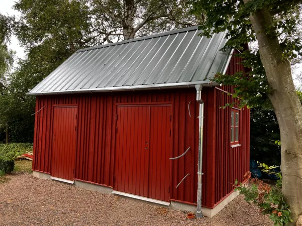 Förråd / snickeri. Faluröd, oregelbunden locklistpanel, cellulosaisolering. Galvad pannplåt.